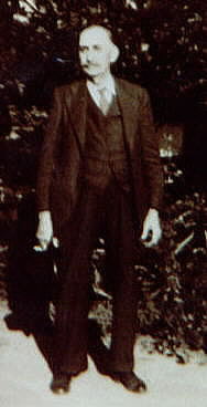 white man standing in front of trees in a dark suit
